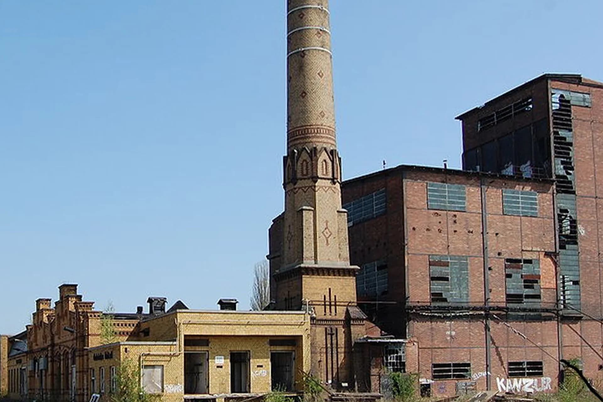 Der denkmalgeschützte Schornstein des RAW-Areals heute — Backsteinruine mit verfallenen Werkhallen, blinden Fenstern und Graffiti