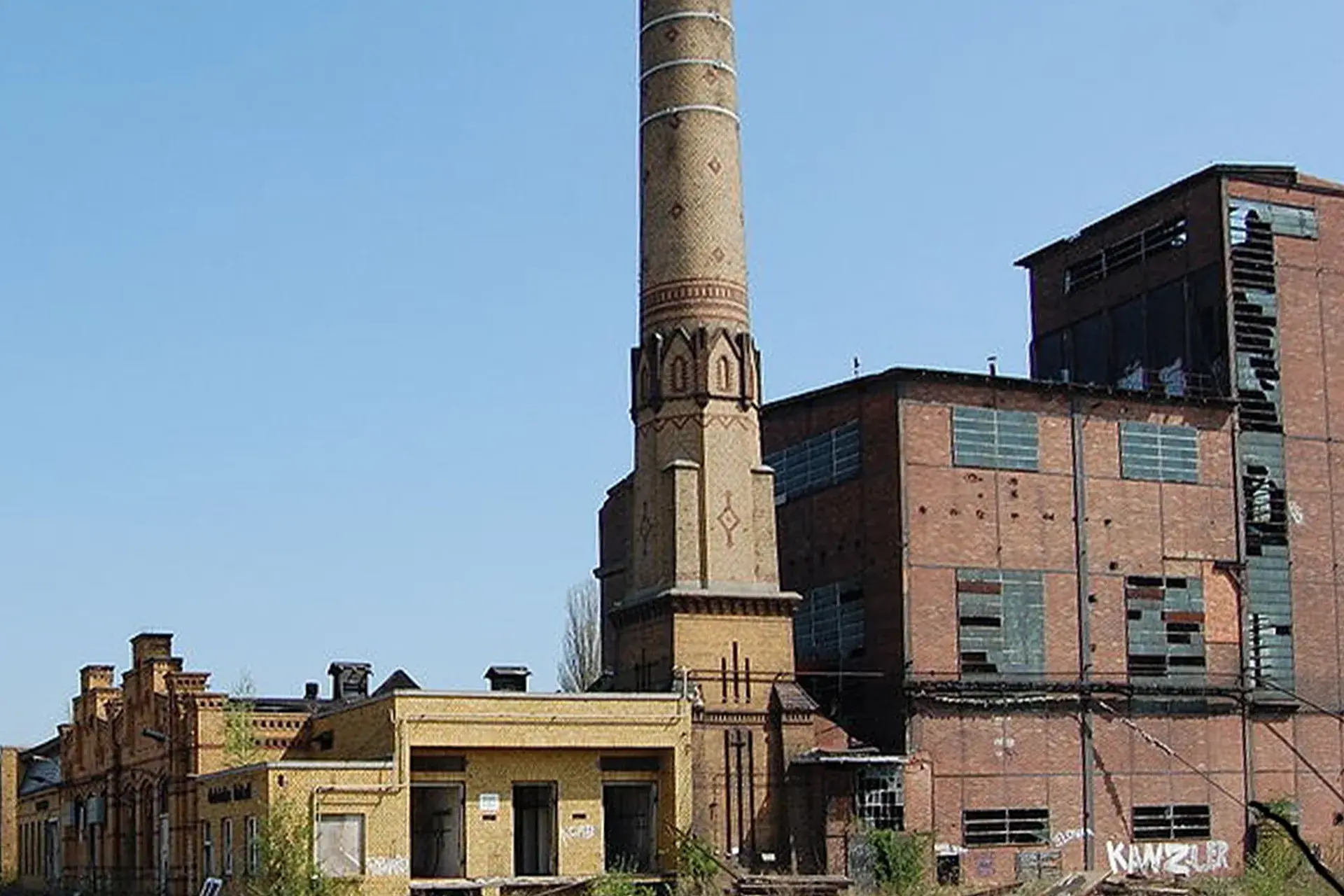 Der denkmalgeschützte Schornstein des RAW-Areals heute — Backsteinruine mit verfallenen Werkhallen, blinden Fenstern und Graffiti